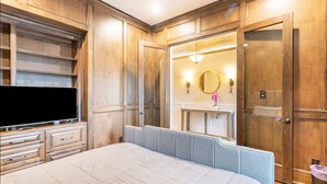 Une chambre à coucher avec un grand lit, une télévision, un lambris en bois, une coiffeuse avec un miroir et une porte.