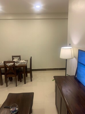 Zona de menjador amb una taula preparada per a quatre persones, un televisor sobre un suport i una làmpada.
