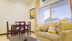 A living room with a dining table, a sofa with patterned cushions, and a large window with a view of a yellow building. - F3 Apartment, 2-Bedroom (F3) (Placencia Village)