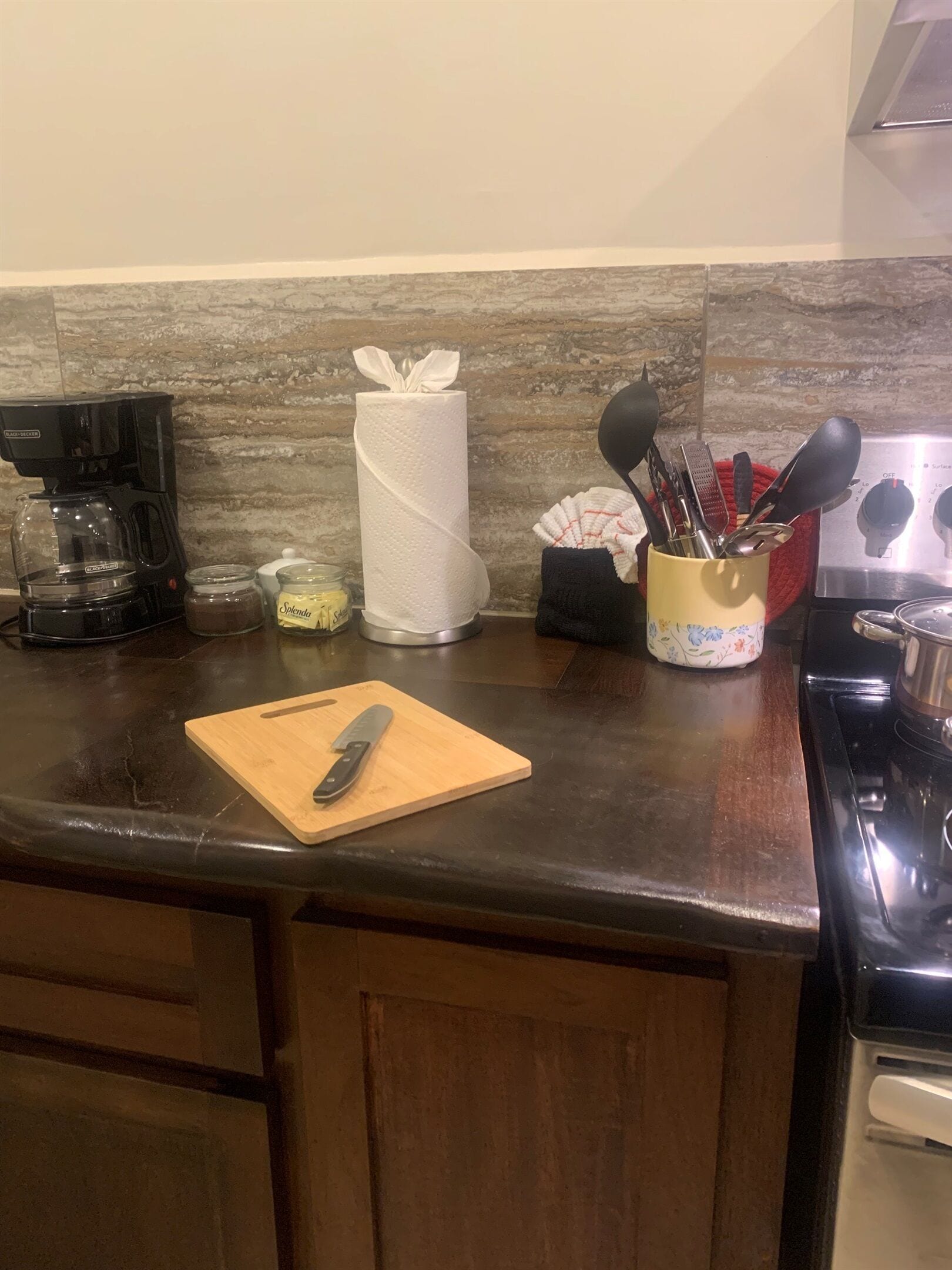 Een keuken met een koffiezetapparaat, een rol keukendoekjes, een snijplank met een mes en een houder voor keukengerei.