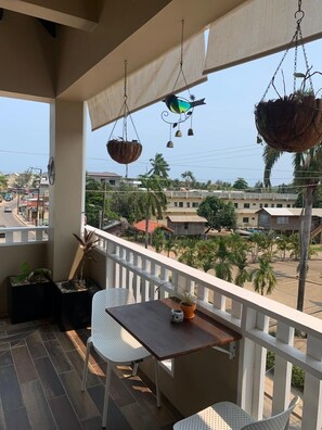 Enjoy a peaceful view of the neighborhood from this balcony with a table, chairs, and a potted plant.