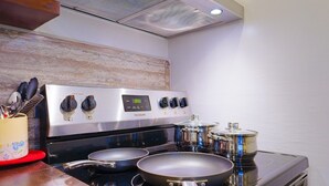 Una cocina con estufa de acero inoxidable, dos sartenes y una olla sobre las hornillas.