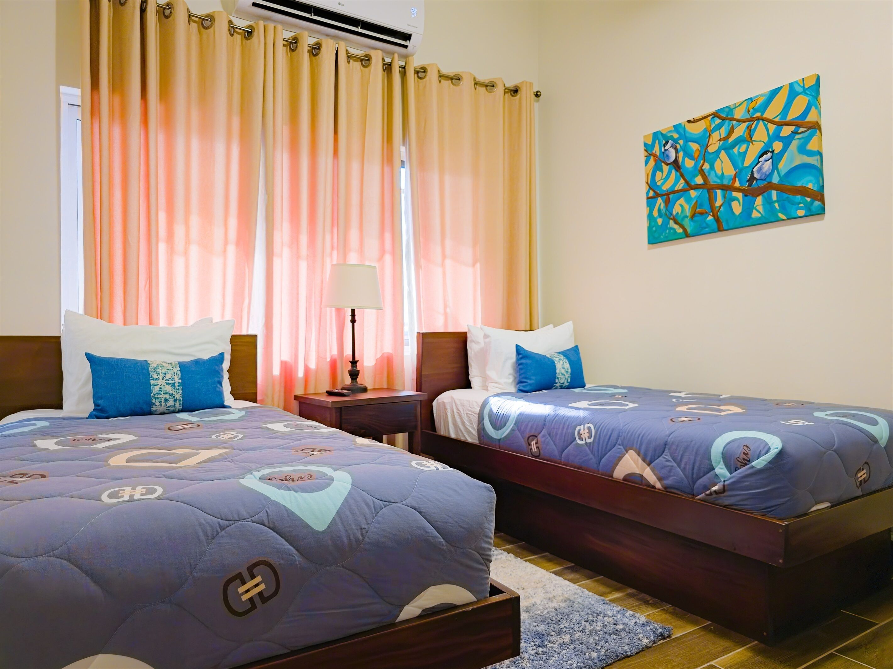 Habitación de hotel con dos camas, una mesita de noche, aire acondicionado y un cuadro en la pared.