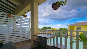 A balcony with a wooden table and two chairs, a hanging plant, and a view of a yellow building.