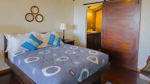 A bedroom with a bed, a nightstand, a lamp, a wooden ceiling, and a sliding door leading to a bathroom.