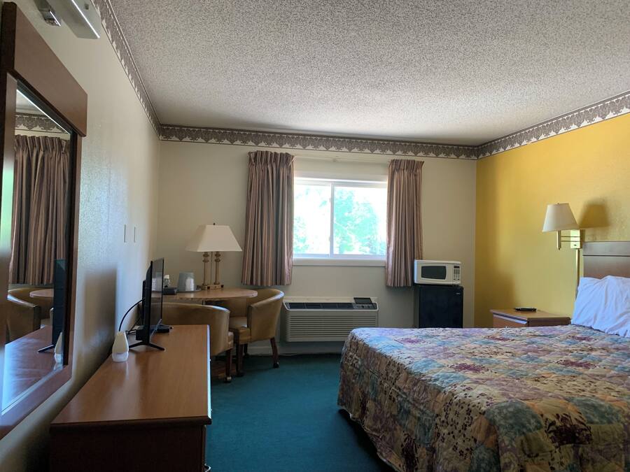 A hotel room with a bed, a desk with a lamp, a microwave, and a window with curtains.