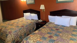 Habitación de hotel con dos camas, cada una con una colcha estampada con motivos florales, una lámpara de noche y un teléfono en la mesita.