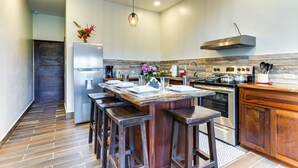 A modern kitchen with a central island, bar stools, a stainless steel refrigerator, and a built-in oven. - T4 Suite, 2-Bedroom (T4) (Placencia Village)