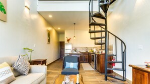 A modern living room with a sofa, a coffee table with glasses and a bottle, a spiral staircase, and a kitchen in the background. - T4 Suite, 2-Bedroom (T4) (Placencia Village)