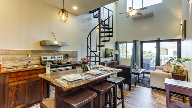 A modern kitchen with a central island, a spiral staircase, and a dining area with a sofa and table. - T4 Suite, 2-Bedroom (T4) (Placencia Village)