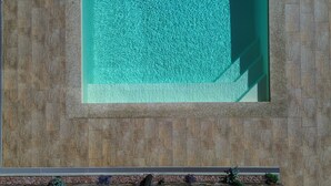 En swimmingpool med klart vatten, omgiven av stenplattor och ett metallräcke.