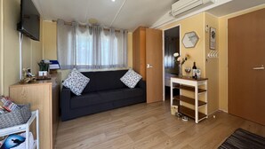 Ett mysigt vardagsrum med en mörk soffa, ett träbord, en tv som är monterad på väggen och ett fönster med gardiner.