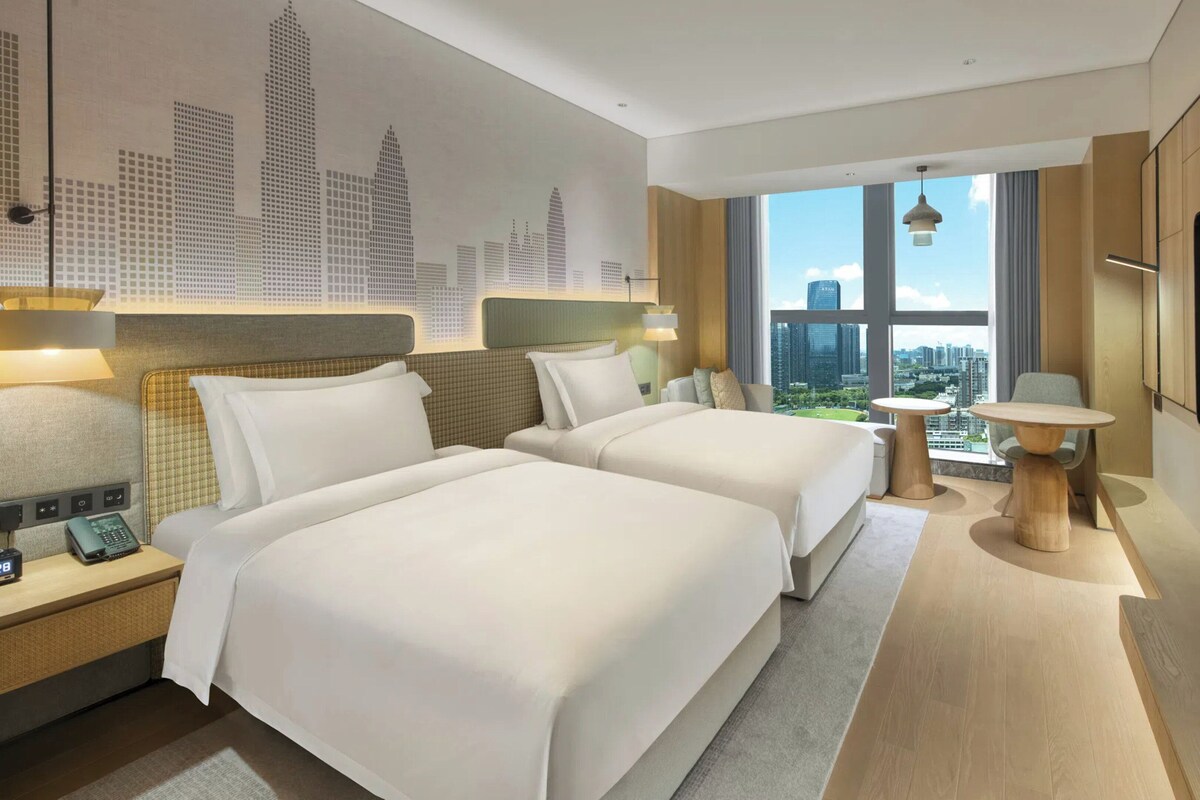 Een moderne hotelkamer met twee bedden, een grote televisie en uitzicht over de stad.
