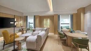 A modern hotel room with a large sofa, dining table, and chairs, a flat-screen TV, and a city view. - Holiday Inn Shenzhen Nanshan by IHG (Shenzhen)