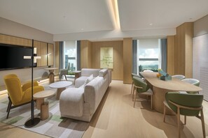 Een moderne hotelkamer met een ruime bank, eettafel en stoelen, een flatscreen televisie en uitzicht op de stad.