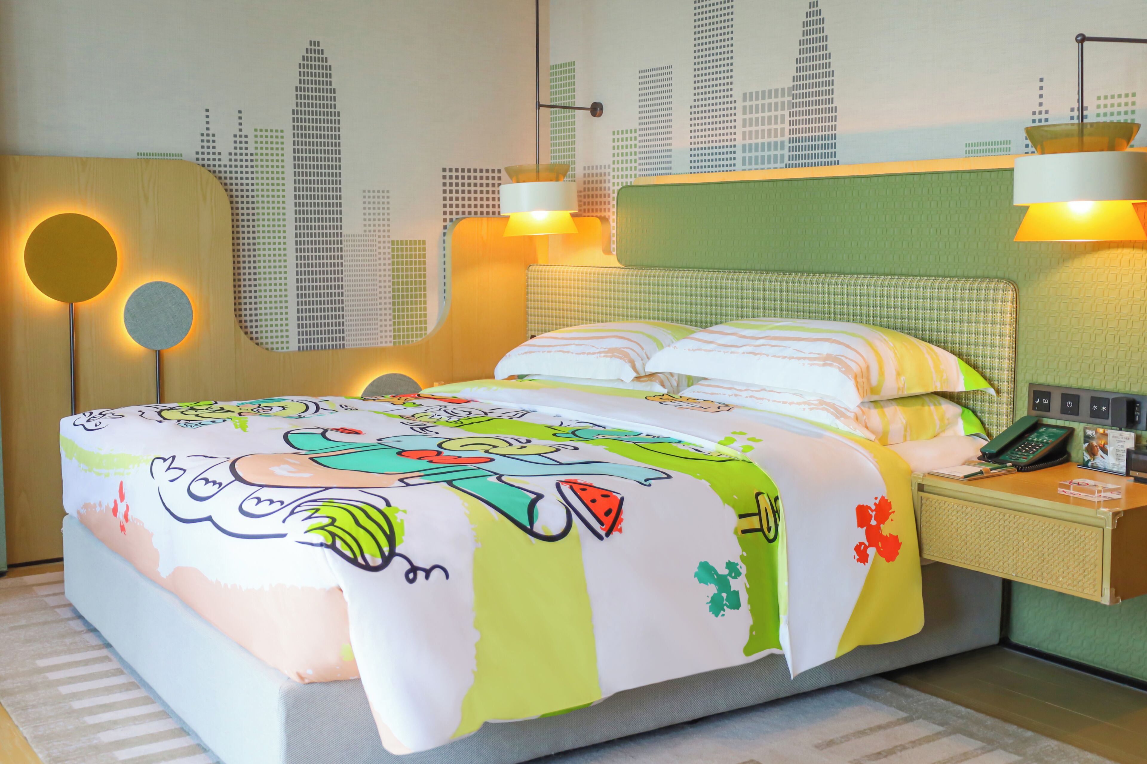Une chambre d’hôtel avec un lit, une table de chevet, un téléphone et une fresque murale représentant un paysage urbain.