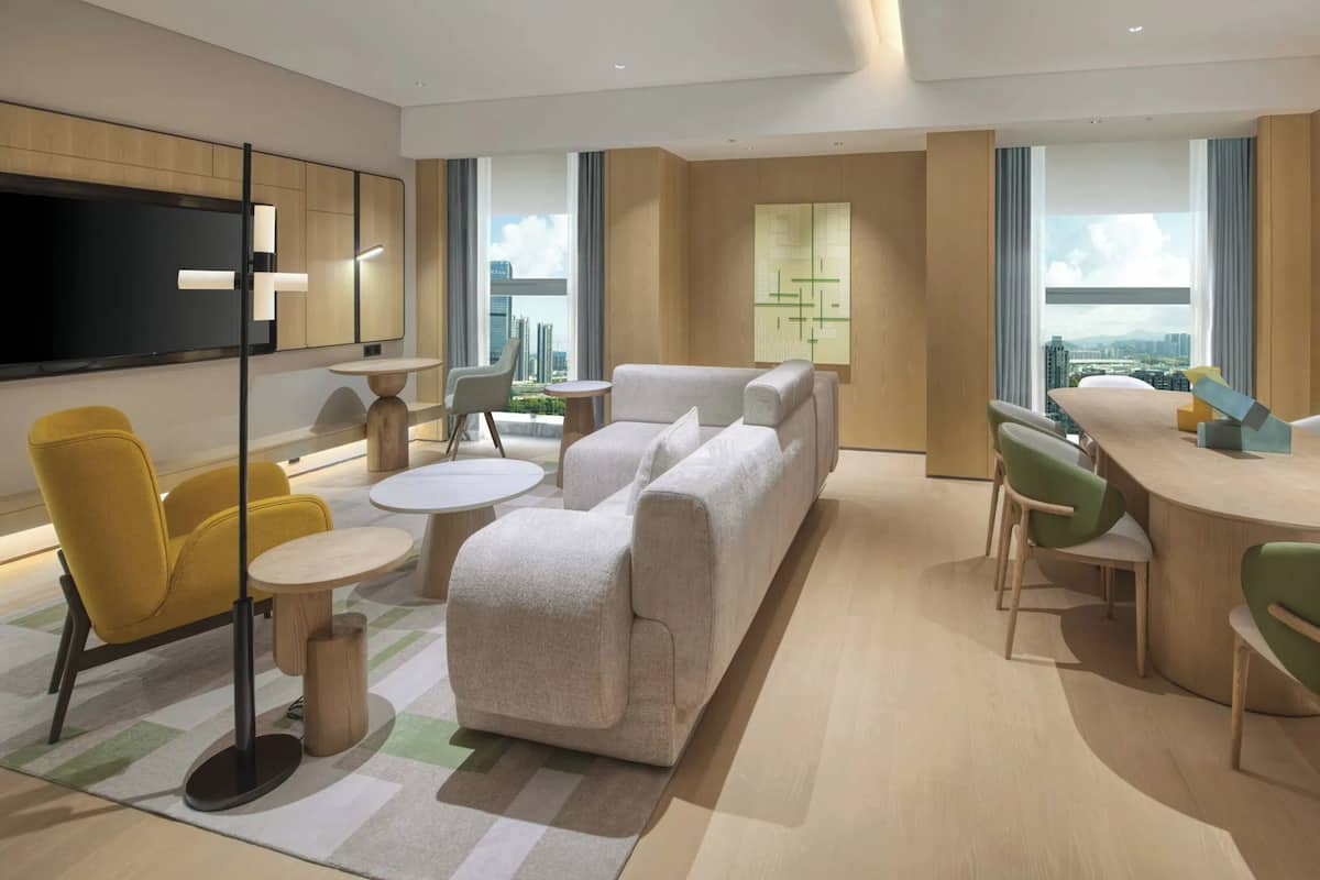 A modern living room with a sofa, yellow chairs, a round table, and a TV.