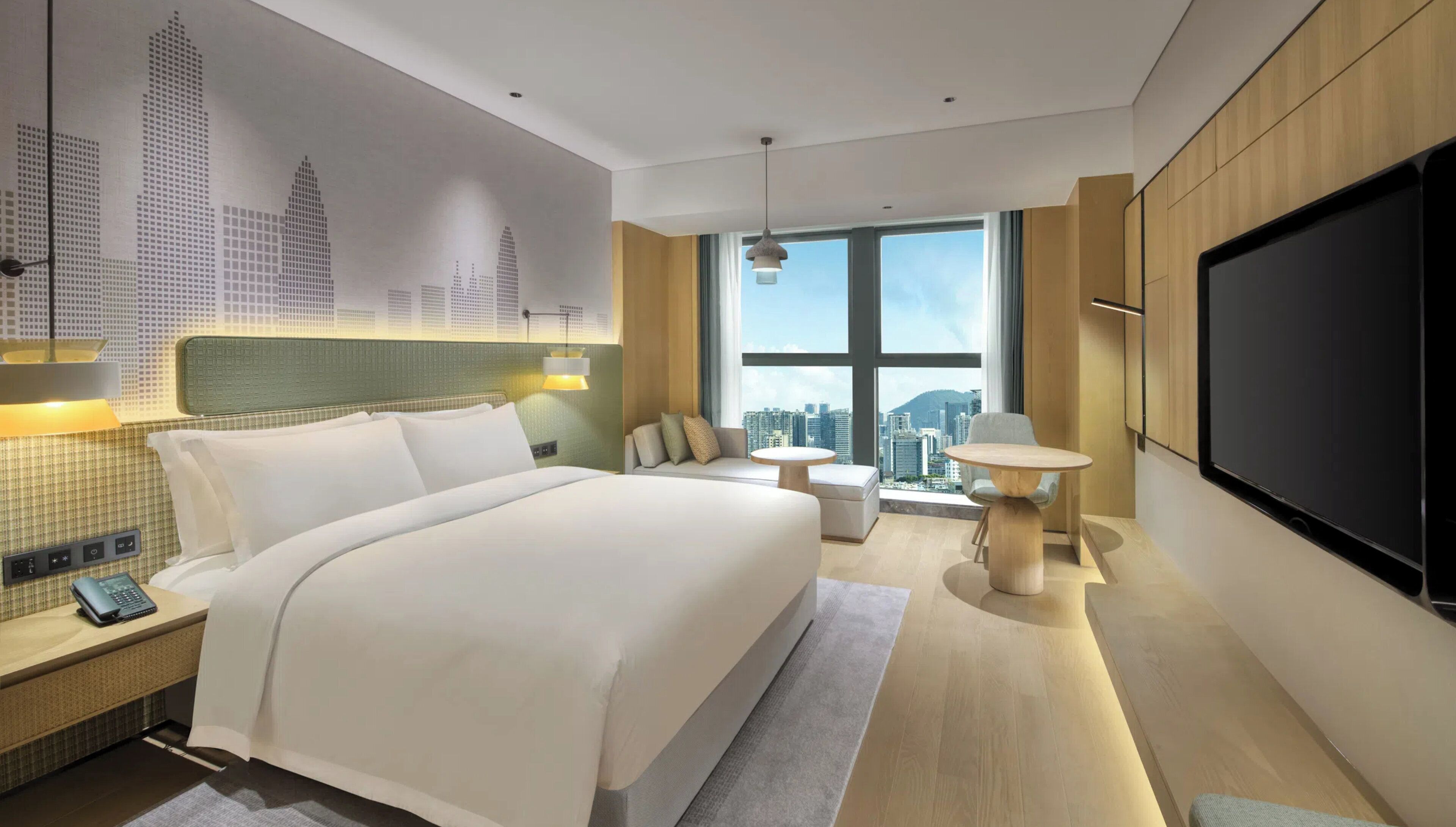 A modern hotel room with a large bed, a TV, a city view, and a small table.
