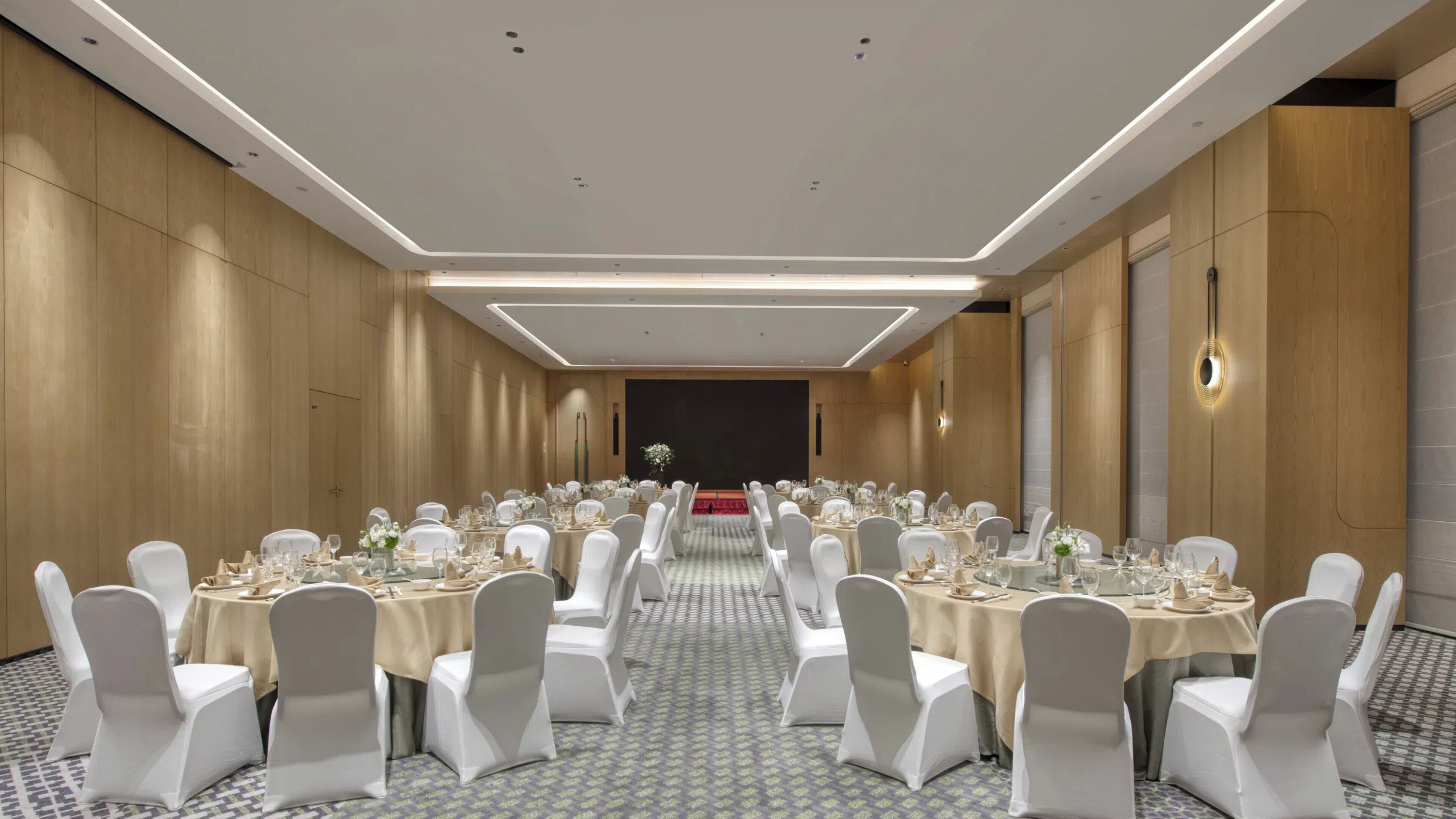 A conference room with round tables, white chairs, and a stage at the front.