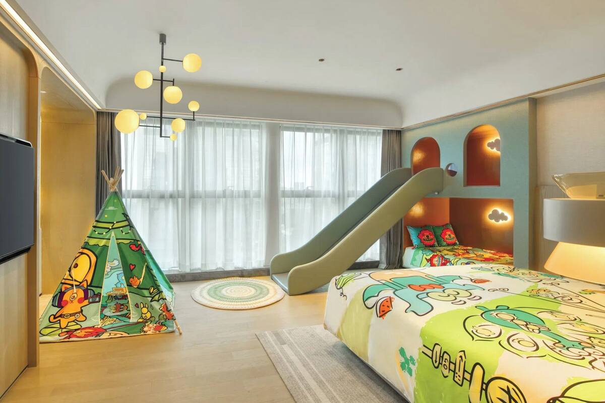 A modern bedroom with a large bed, a flat-screen TV, a slide, and a colorful tent.