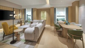Een moderne woonkamer met een bank, gele stoelen, een ronde tafel en een televisie.