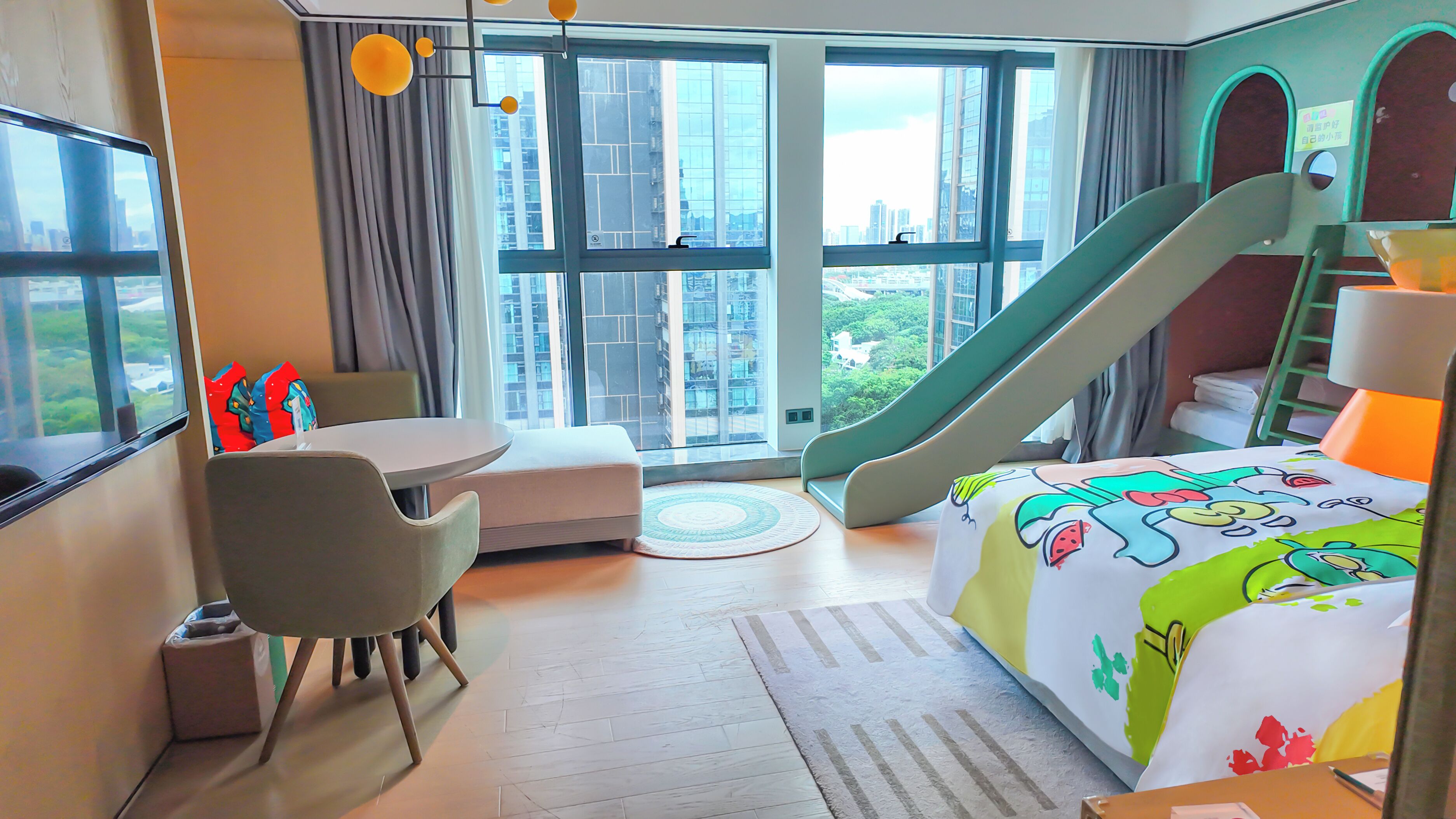 Quarto de hotel com cama, escrivaninha, cadeira, mesa pequena, sofá, janela com vista para edifícios e um escorrega.