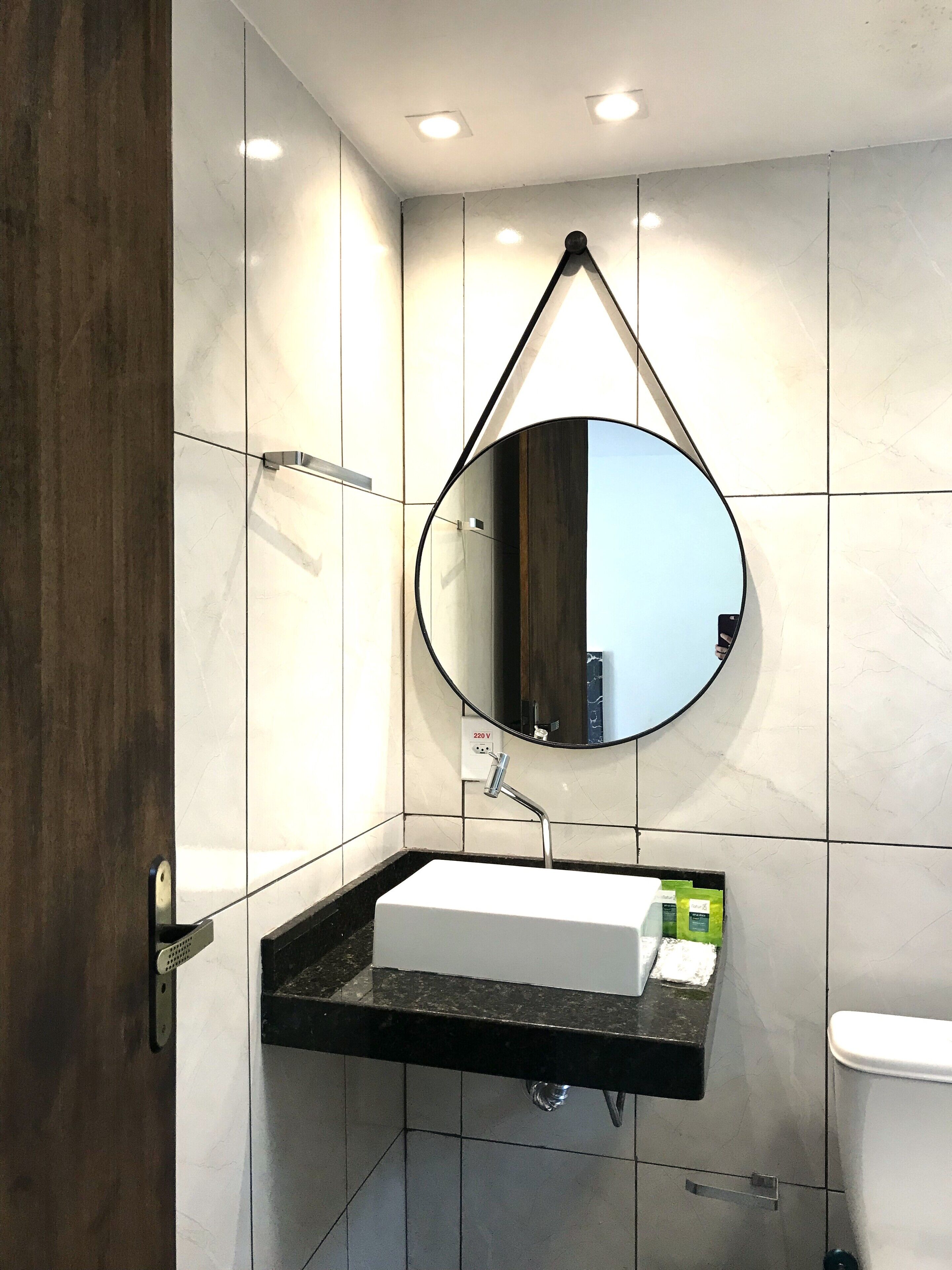 Un baño moderno con un lavabo blanco, un espejo redondo y una encimera negra.