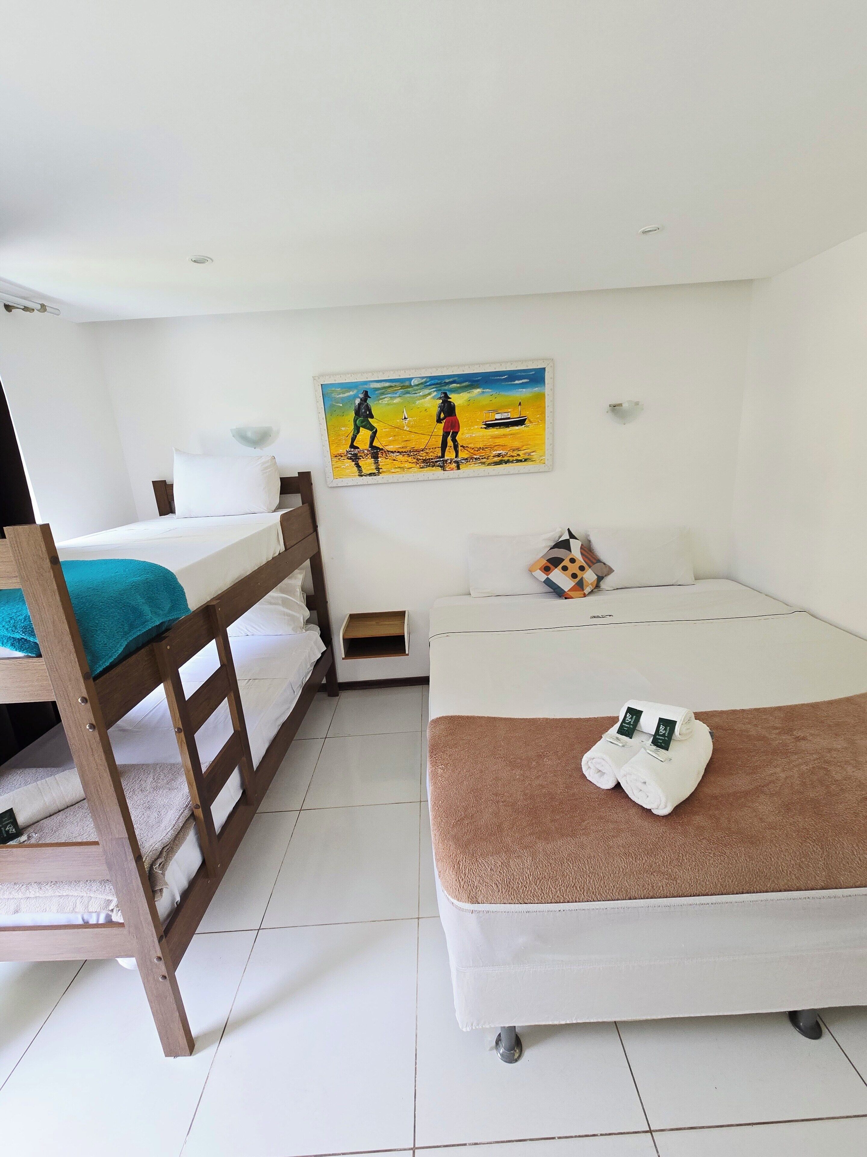 A room with a bunk bed, a single bed, a painting, and a small wooden shelf.