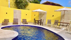 A swimming pool with lounge chairs and umbrellas, surrounded by yellow walls. - Pousada Gente Bonita La Mansion (Búzios)