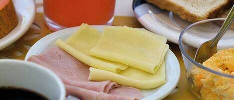 A breakfast setting with bread, cheese, ham, a glass of juice, and a cup of coffee on a table with a yellow tablecloth.