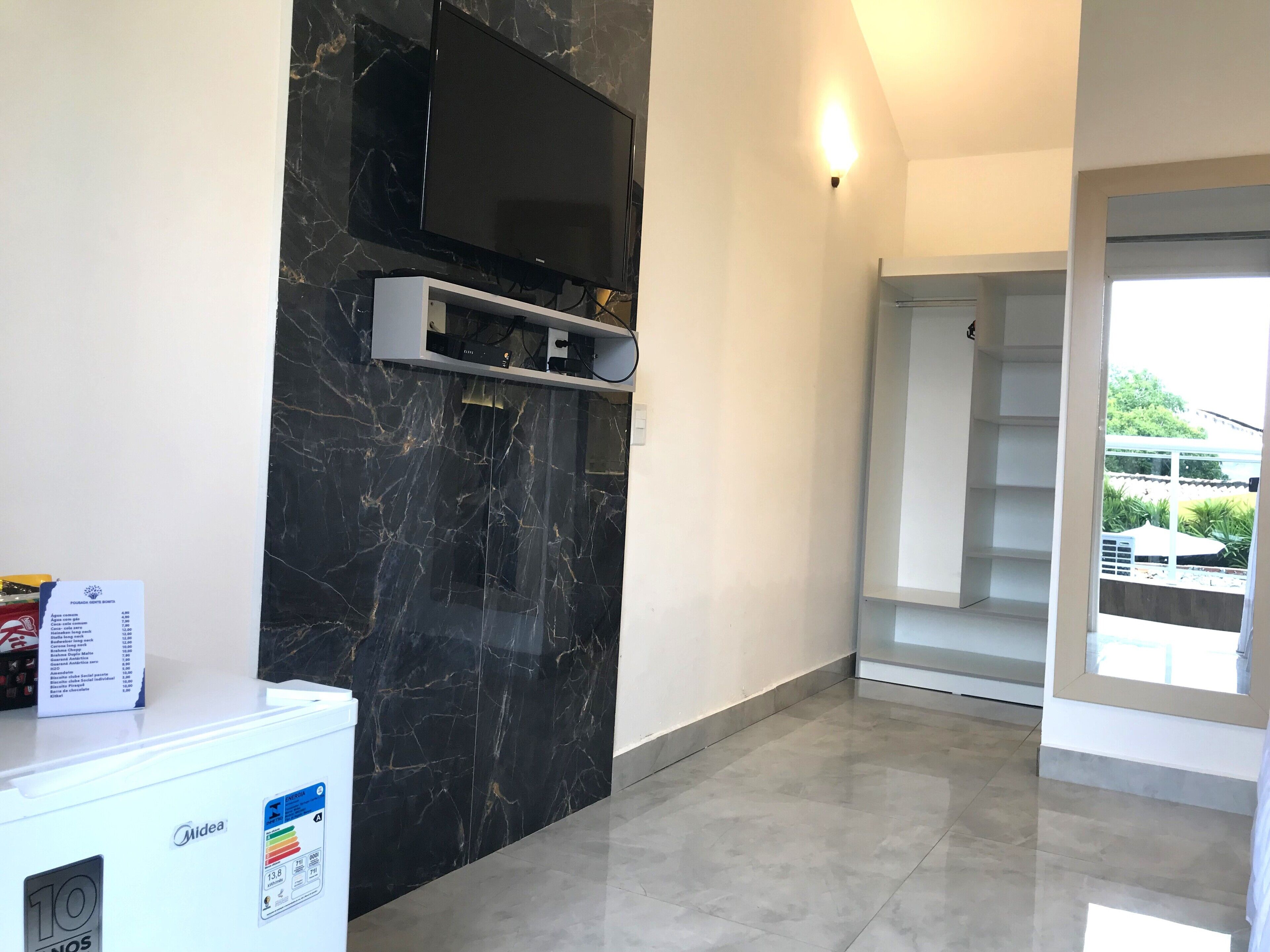 Una sala moderna con una pared de mármol negro, un televisor de pantalla plana montado sobre un mueble blanco de entretenimiento, y un refrigerador compacto a la izquierda.