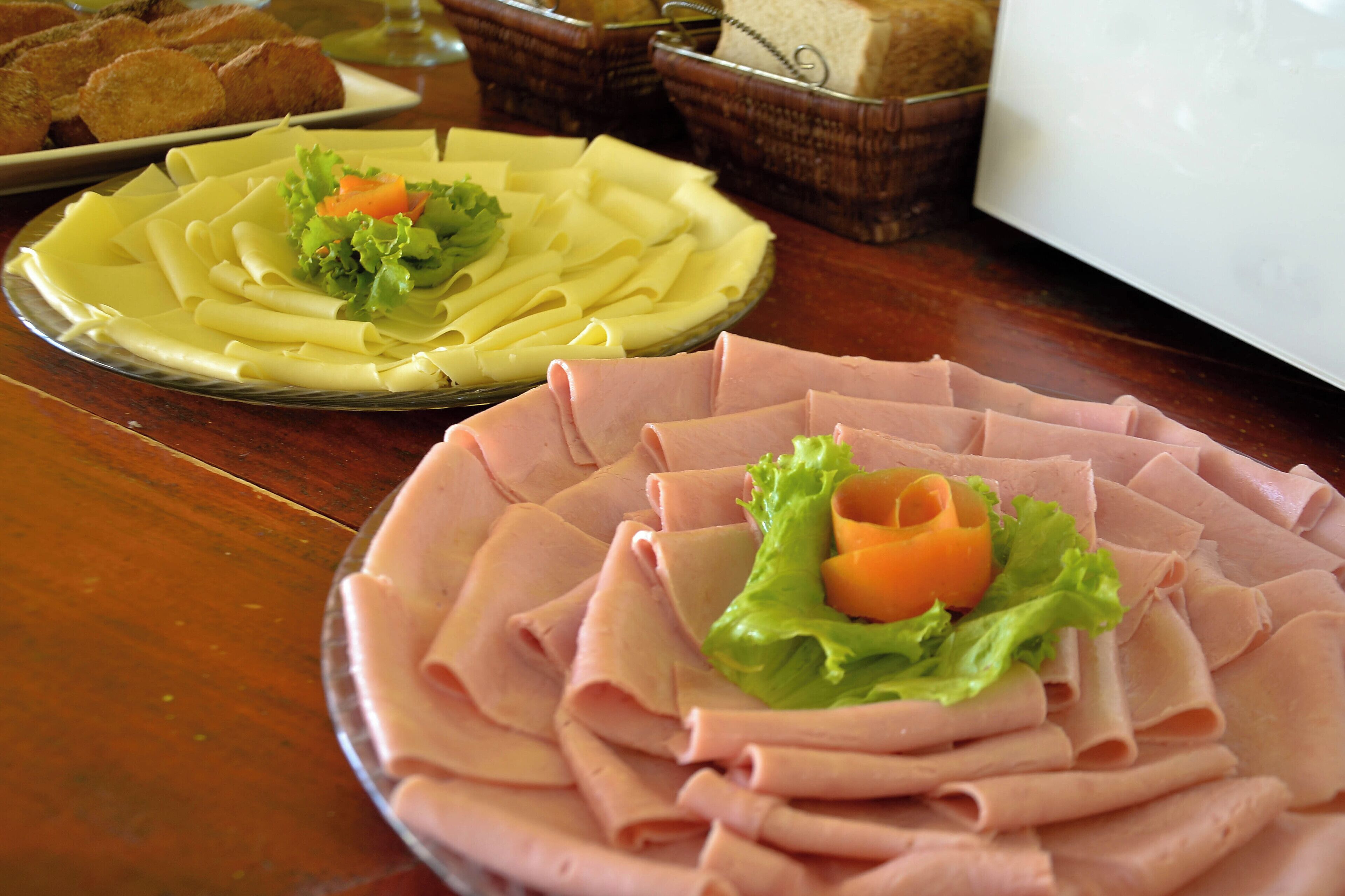 A table with neatly arranged food items, including sliced ham and pasta, and some bread.