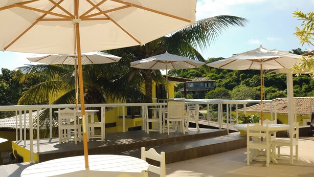 A terrace with white furniture and umbrellas, surrounded by lush greenery. - Pousada Gente Bonita La Mansion (Búzios)