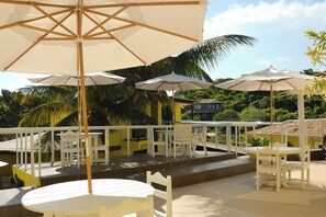 A terrace with white furniture and umbrellas, surrounded by lush greenery. - Pousada Gente Bonita La Mansion (Búzios)