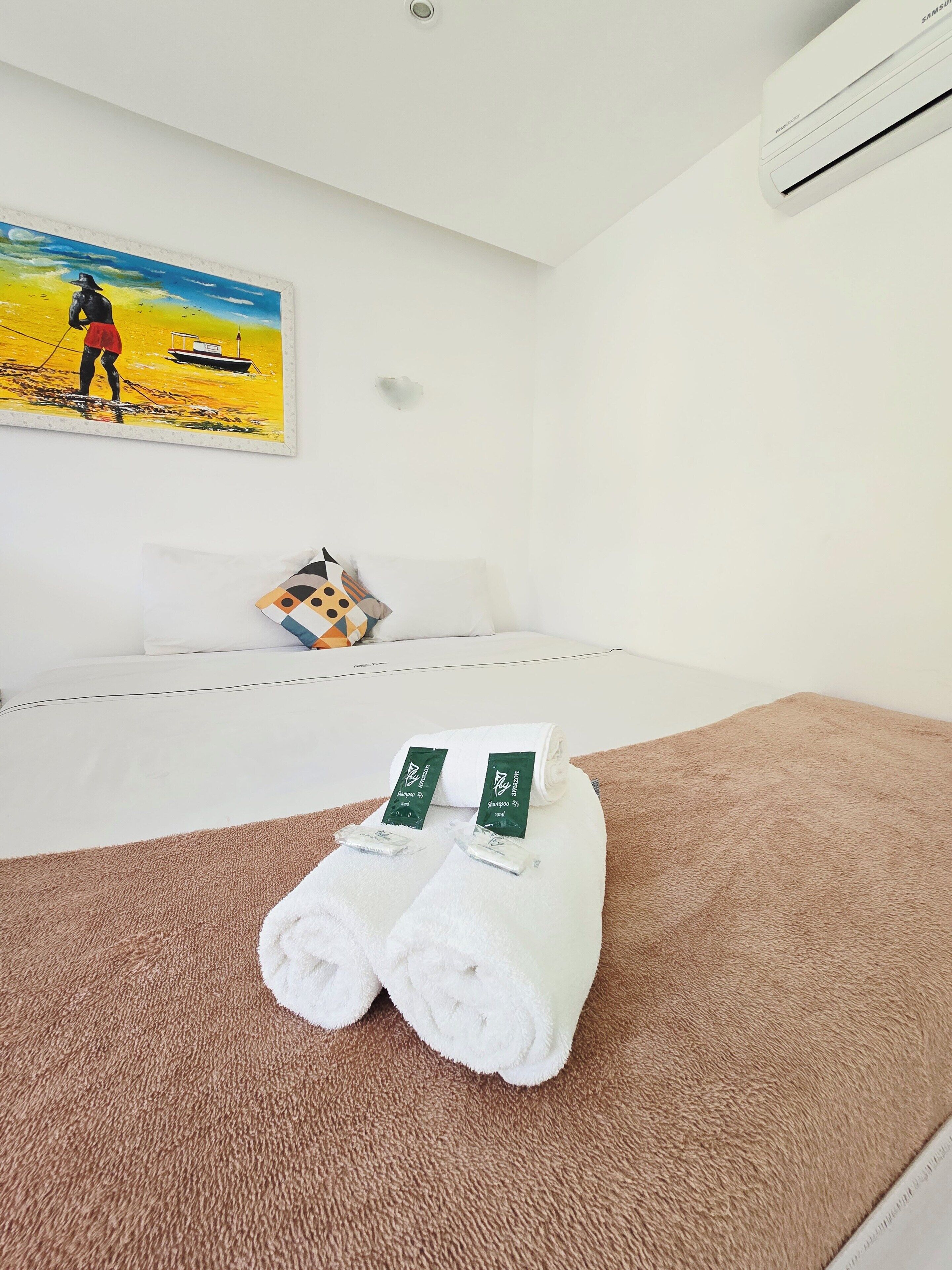 A hotel room with a bed, a painting, a pillow, and a brown carpet.