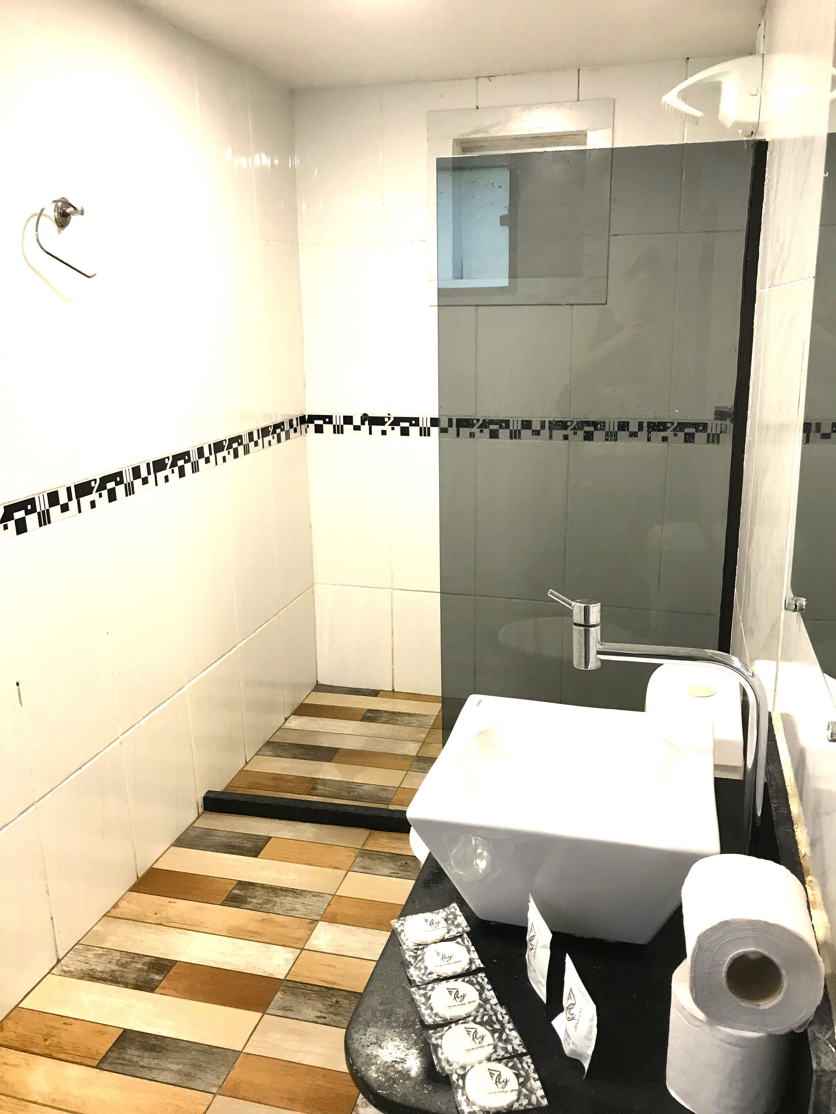 A bathroom with a tiled floor, a shower, a sink, and toilet paper.