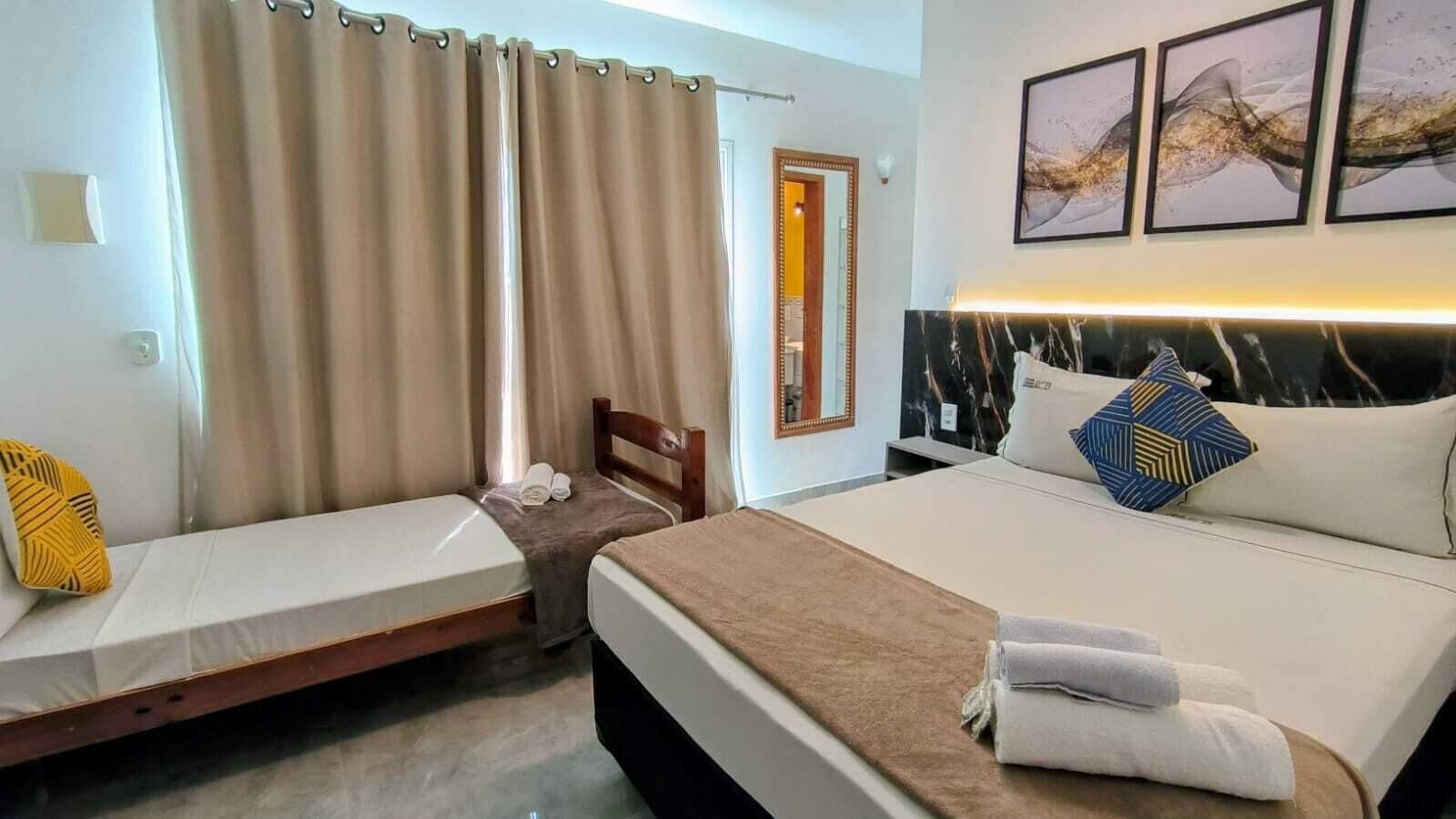 A hotel room with two beds, a headboard, a bedside table, a mirror, and artwork on the wall.