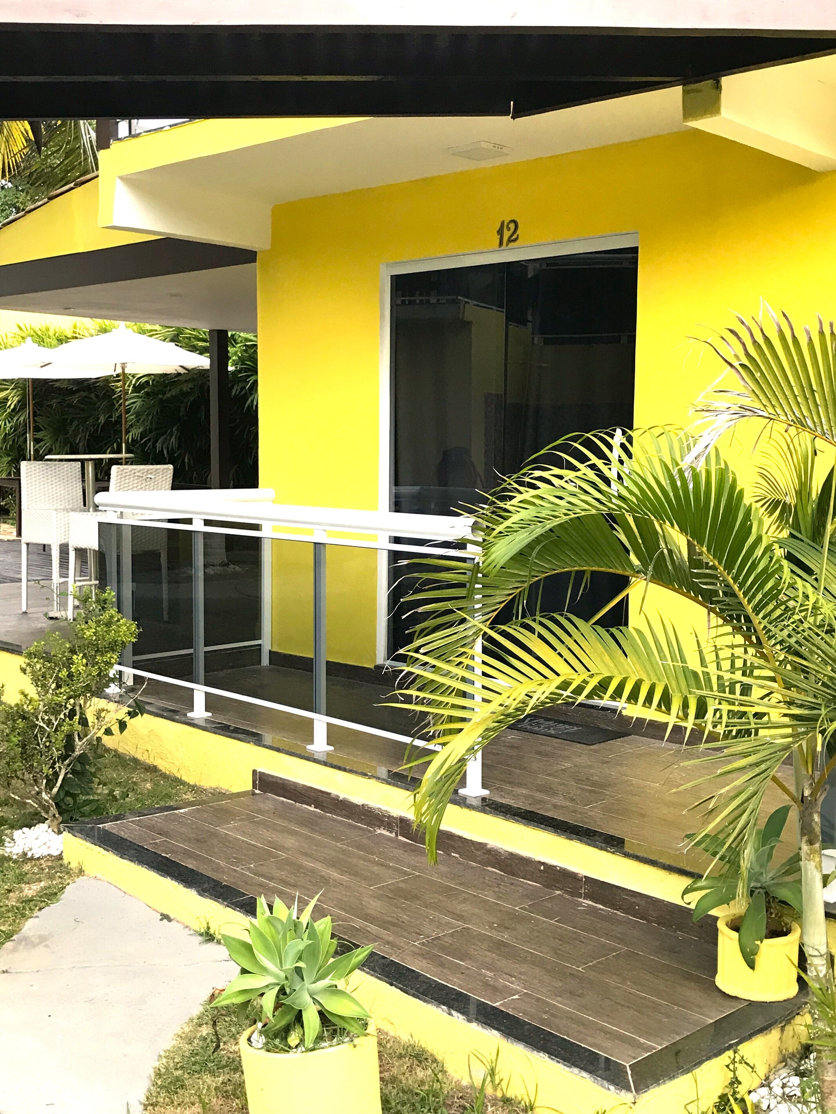 A yellow building with a balcony, a door marked with the number 12, and potted plants.