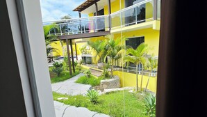 A yellow building with a balcony, a stone pathway, and various plants. - Pousada Gente Bonita La Mansion (Búzios)