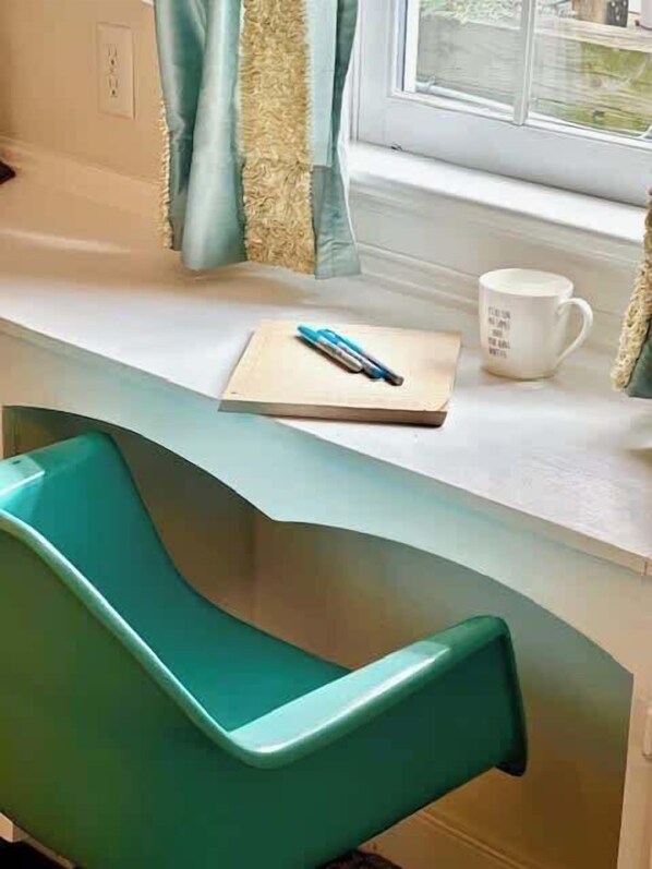 Ein blaugrüner Sessel, ein weißer Schreibtisch, eine blaue Tasse und ein Stift auf dem Schreibtisch.