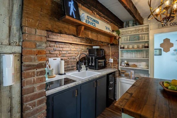 A kitchen with a brick wall, a coffee machine, a sink, and a sign for 'Stomper Service'.