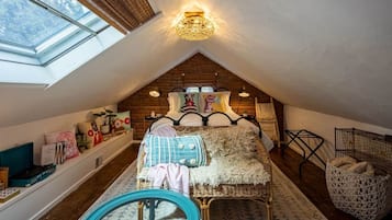 Een knus slaapkamer onder het dak, met een schuine hemel, een bed met decoratief hoofdeinde, een dakraam en een rieten stoel.