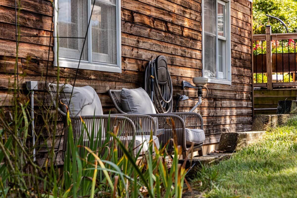 Un rustico chalet in legno con un'area relax sul portico, un tubo da giardino e una recinzione in legno.