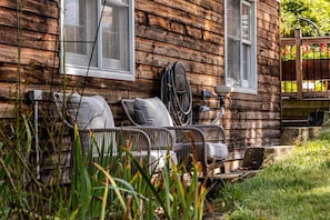A rustic wooden cabin with a porch seating area, a hose, and a wooden fence.