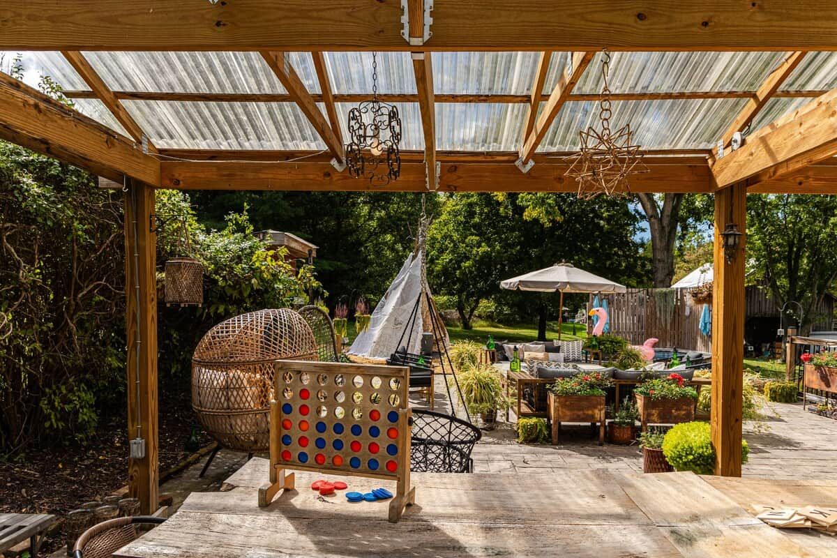 Un patio couvert agrémenté d’une pergola en bois, de sièges d’extérieur et d’un espace dédié aux jeux de société.