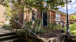 Ein Backsteinhaus mit einer Holztür, einer kleinen Veranda und einem Garten mit Stufen zum Eingang.