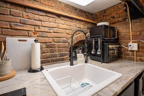 Une cuisine dotée d’un plan de travail en marbre, d’un évier avec un distributeur de savon et d’une machine à café.
