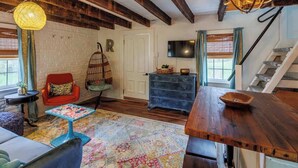 Ein gemütliches Wohnzimmer mit Holzbalkendecke, einem roten Sessel, einem blauen Tisch und einem farbenfrohen Teppich.