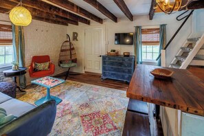 A cozy living room with a wooden ceiling, a red chair, a blue table, and a colorful rug.