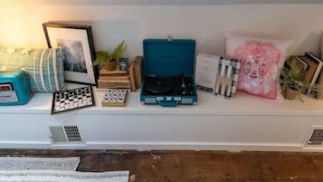 Una estantería con varios objetos, incluyendo un reproductor de casetes, un cuadro enmarco, libros y cojines decorativos.